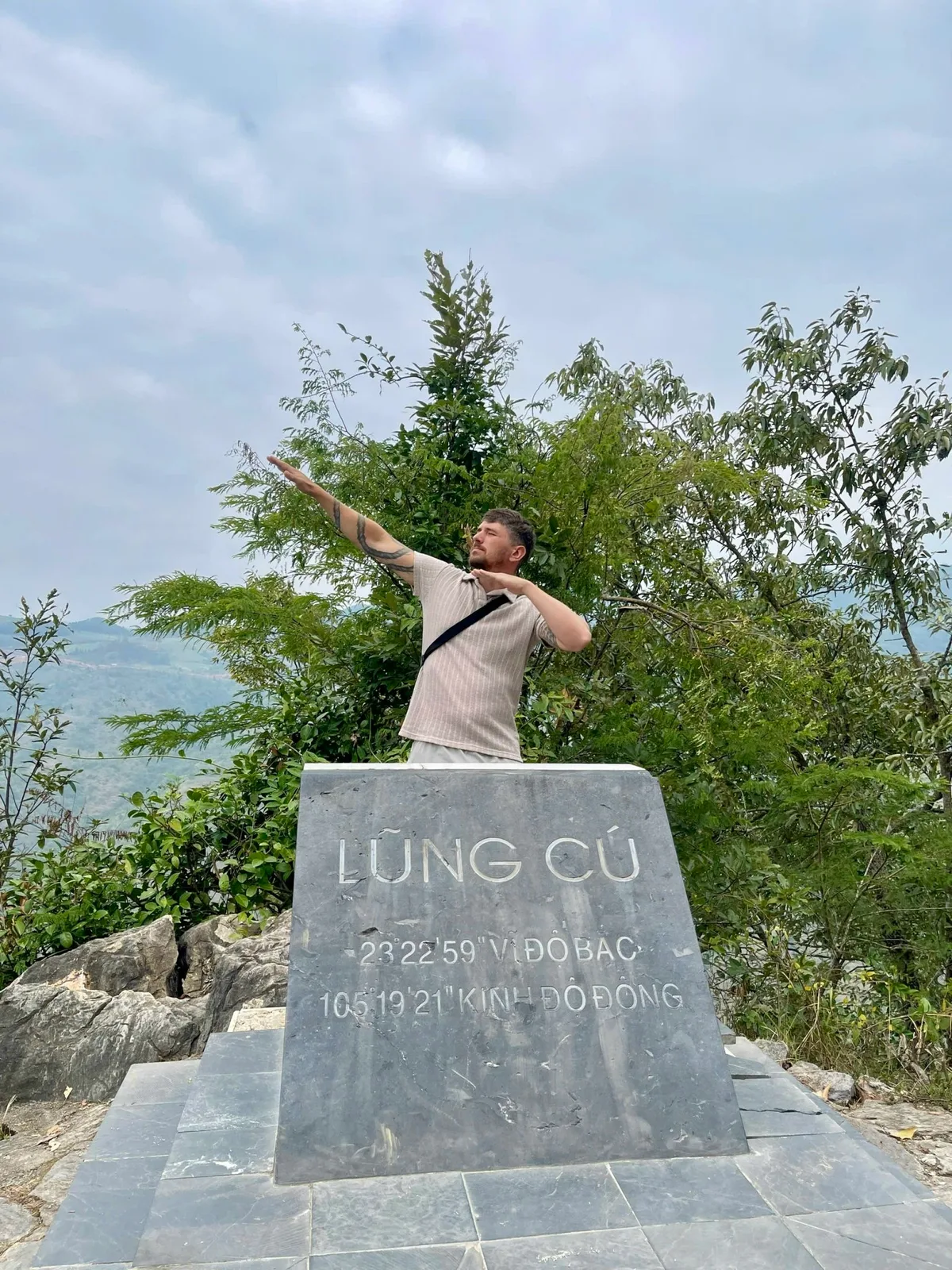 Guest posing behind the Lung Cu marker stone with its northern latitude coordinates in Ha Giang