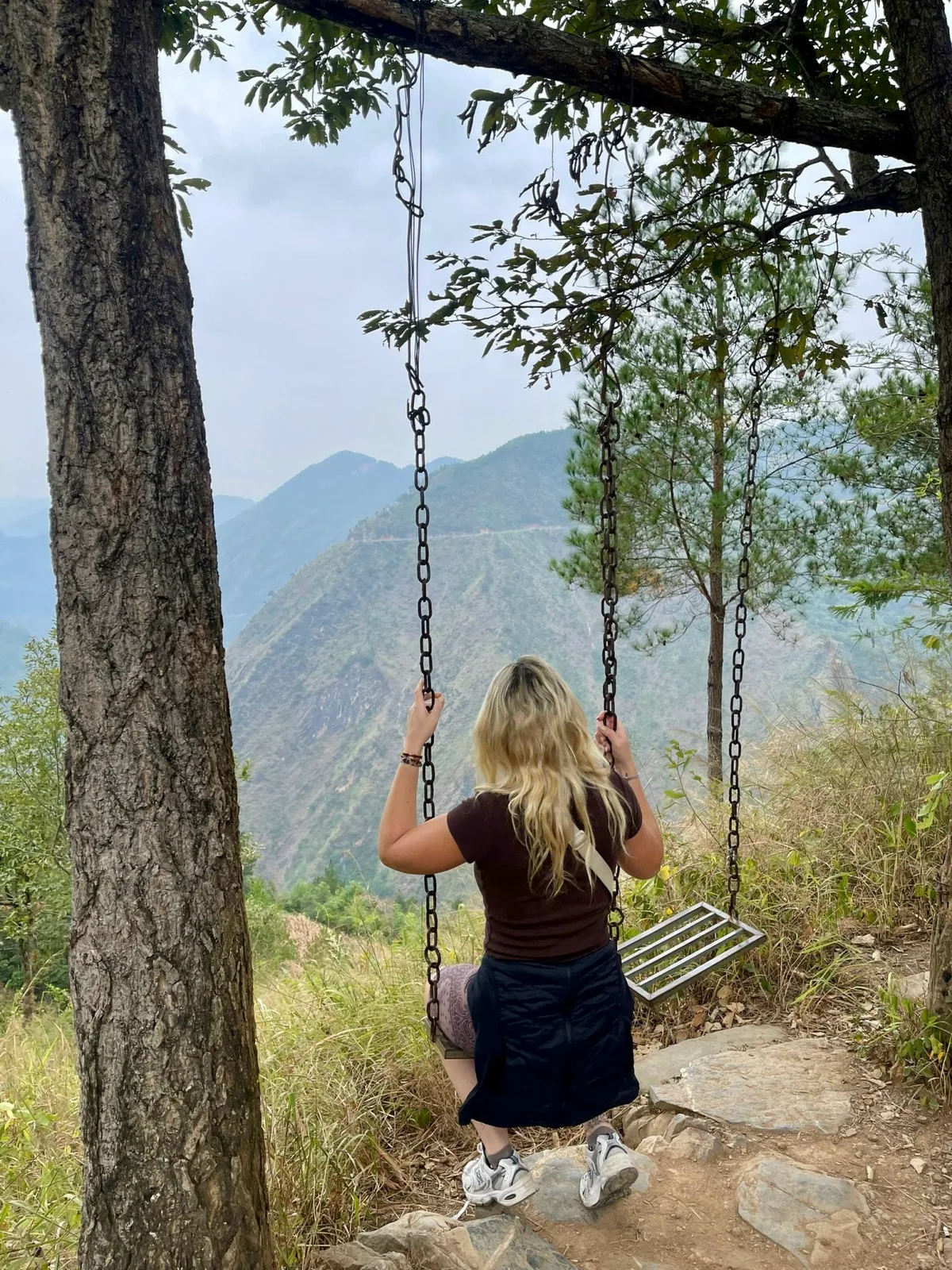 Guest on a tree swing looking out over the mountains and a winding road in Ha Giang