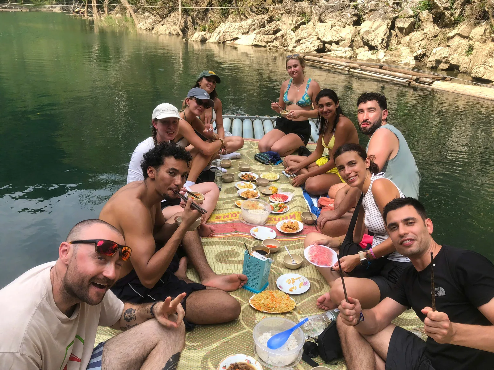 Group of friends sharing lunch on a bamboo raft on a calm green river in Ha Giang