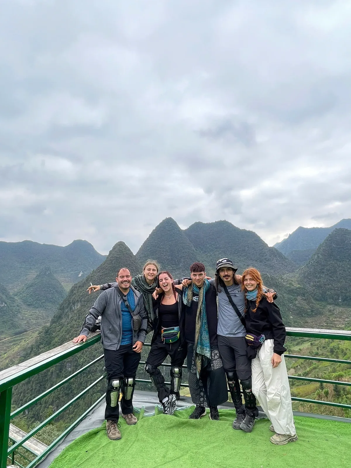 Riders wearing knee pads at a karst mountain viewpoint on a cloudy day in Ha Giang