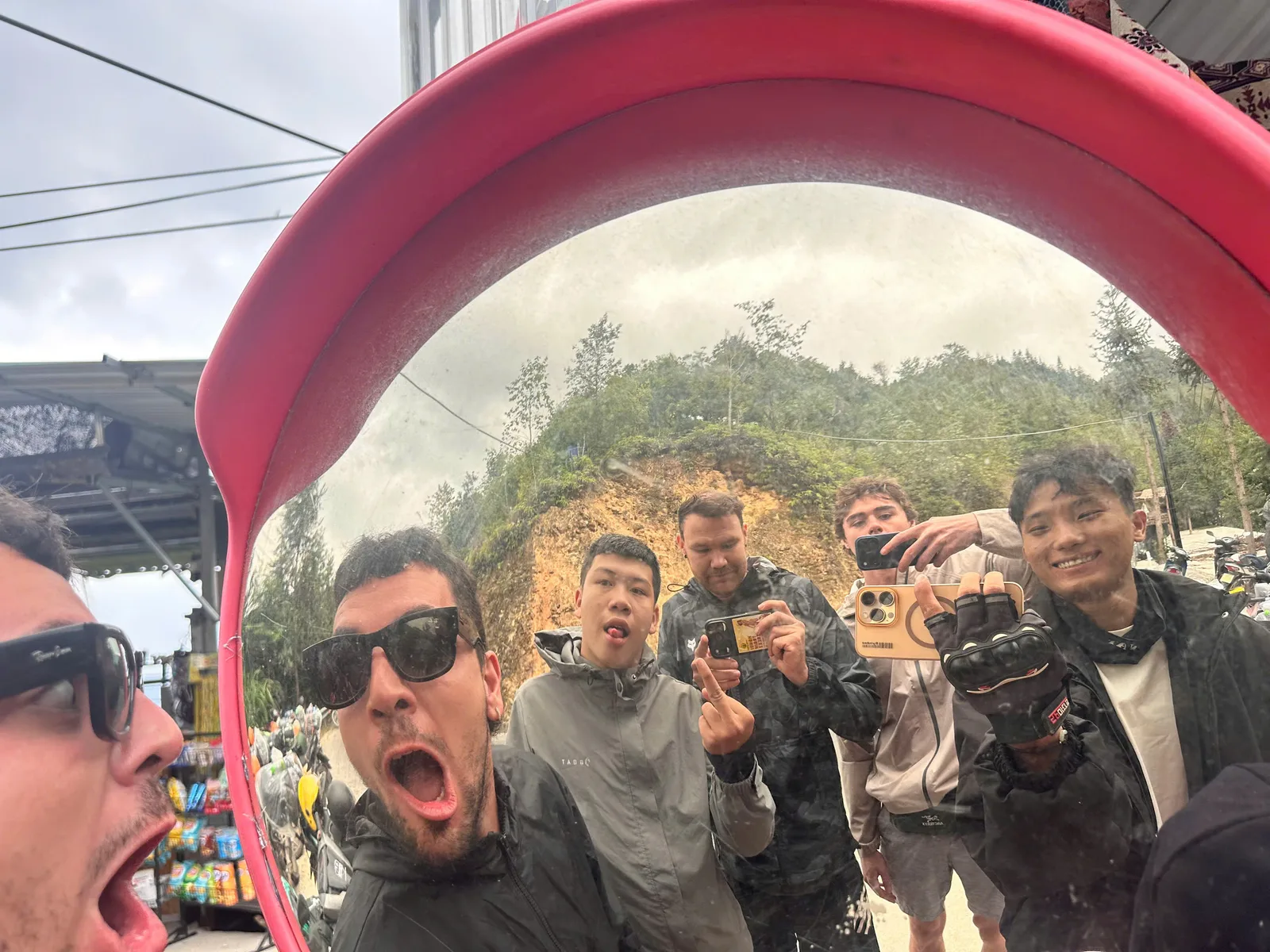 Friends taking a funny selfie in a roadside traffic mirror during a Ha Giang Loop riding day